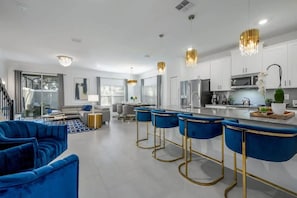 A modern kitchen with white cabinets, a central island, and blue bar stools. - Storey Lake 5BR w/ Pool + Themed Rooms Near Disney (Kissimmee)