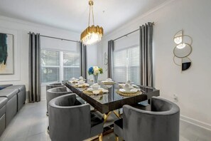 A modern dining room with a long table, grey upholstered chairs, and a chandelier. - Storey Lake 5BR w/ Pool + Themed Rooms Near Disney (Kissimmee)
