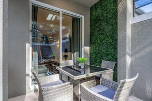 A balcony with wicker furniture and a glass table, a green wall, and a view of the interior. - Storey Lake 5BR w/ Pool + Themed Rooms Near Disney (Kissimmee)