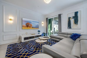 Un salon moderne avec un grand canapé, un téléviseur à écran plat et des œuvres d’art accrochées aux murs.
