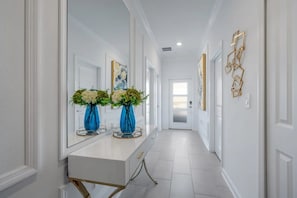 A hallway with a white vanity, two blue vases with flowers, and gold geometric wall art. - Storey Lake 5BR w/ Pool + Themed Rooms Near Disney (Kissimmee)