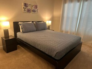 A neatly made bed with a quilted grey duvet, two bedside lamps on matching nightstands, and a pair of floral wall art pieces above the bed. - 4BR Home / Private Pool Near Disney / Storey Lake (Kissimmee)