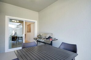 A balcony with a table and chairs, a grill, and a sliding glass door leading to an interior space. - 4BR w/ Private Pool Storey Lake Resort (Kissimmee)