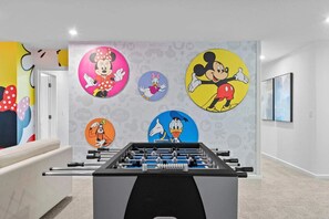 A room with a foosball table and a wall decorated with cartoon characters. - Magical 9BR Retreat w/ Pool & Game Rooms (Kissimmee)
