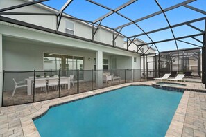 A swimming pool with a glass enclosure, white outdoor furniture, and a covered patio area. - Magical 9BR Retreat w/ Pool & Game Rooms (Kissimmee)