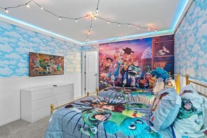 A bedroom with a bed featuring a colorful blanket with cartoon characters, a wall mural of animated characters, and string lights. - Magical 9BR Retreat w/ Pool & Game Rooms (Kissimmee)