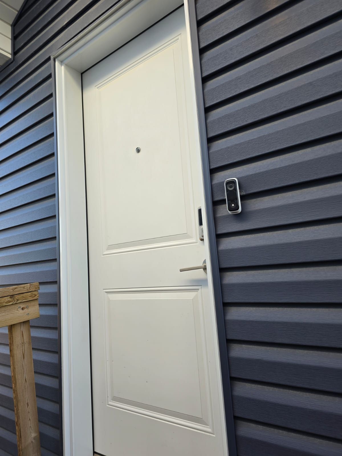A white door with a small peephole and a doorbell button on a gray siding wall.