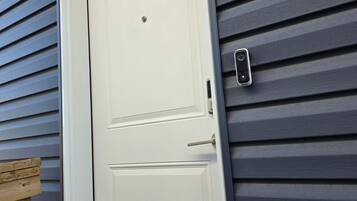 A white door with a small peephole and a doorbell button on a gray siding wall.