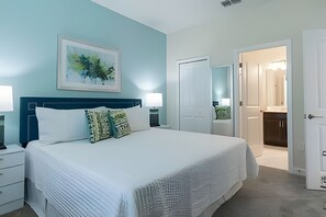 A bedroom with a large bed, a nightstand, a bedside table, a framed picture on the wall, and a door leading to a bathroom. - Spacious 8BR Retreat With Private Pool at CG (Davenport)