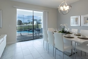 A modern dining area with a glass door leading to a pool, white furniture, and a chandelier. - Spacious 8BR Retreat With Private Pool at CG (Davenport)