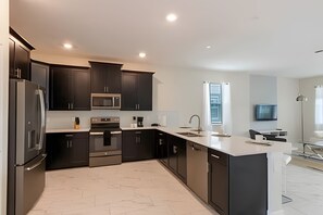 A modern kitchen with dark cabinets, stainless steel appliances, a large island, and a window providing natural light. - Spacious 8BR Retreat With Private Pool at CG (Davenport)