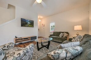 A living room with a sofa, a coffee table, a TV, and a patterned rug. - 4BR Townhome W/pool Near Disney (Kissimmee)