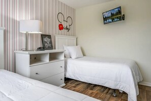 A hotel room with two beds, a bedside table with a lamp, a framed picture on the wall, and a television mounted on the wall. - 4BR Townhome W/pool Near Disney (Kissimmee)