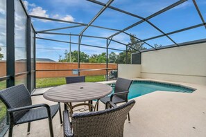 A covered outdoor area with a pool, a table, and chairs. - 4BR Townhome W/pool Near Disney (Kissimmee)