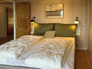 Ein Bett mit weißer Decke und Kissen, eine Holztür und ein gerahmtes Bild an der Wand.