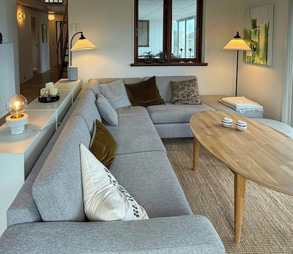 A modern living room with a grey sectional sofa, a wooden coffee table, and two floor lamps. - Sandager Næs holiday home, beach 30 m away (Assens)