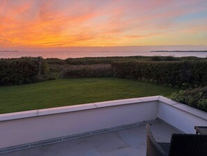 A rooftop terrace with a view of the sunset over the sea, a grassy lawn, and a white railing. - Sandager Næs holiday home, beach 30 m away (Assens)