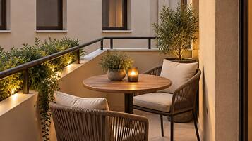 A modern outdoor seating area with two wicker chairs and a round table, surrounded by potted plants and a railing.