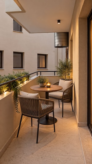 A modern outdoor seating area with two wicker chairs and a round table, surrounded by potted plants and a railing. - ROI House (Athina)