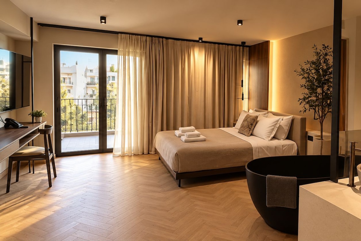 A modern hotel room with a bed, a desk, a large mirror, and a bathroom with a double sink.