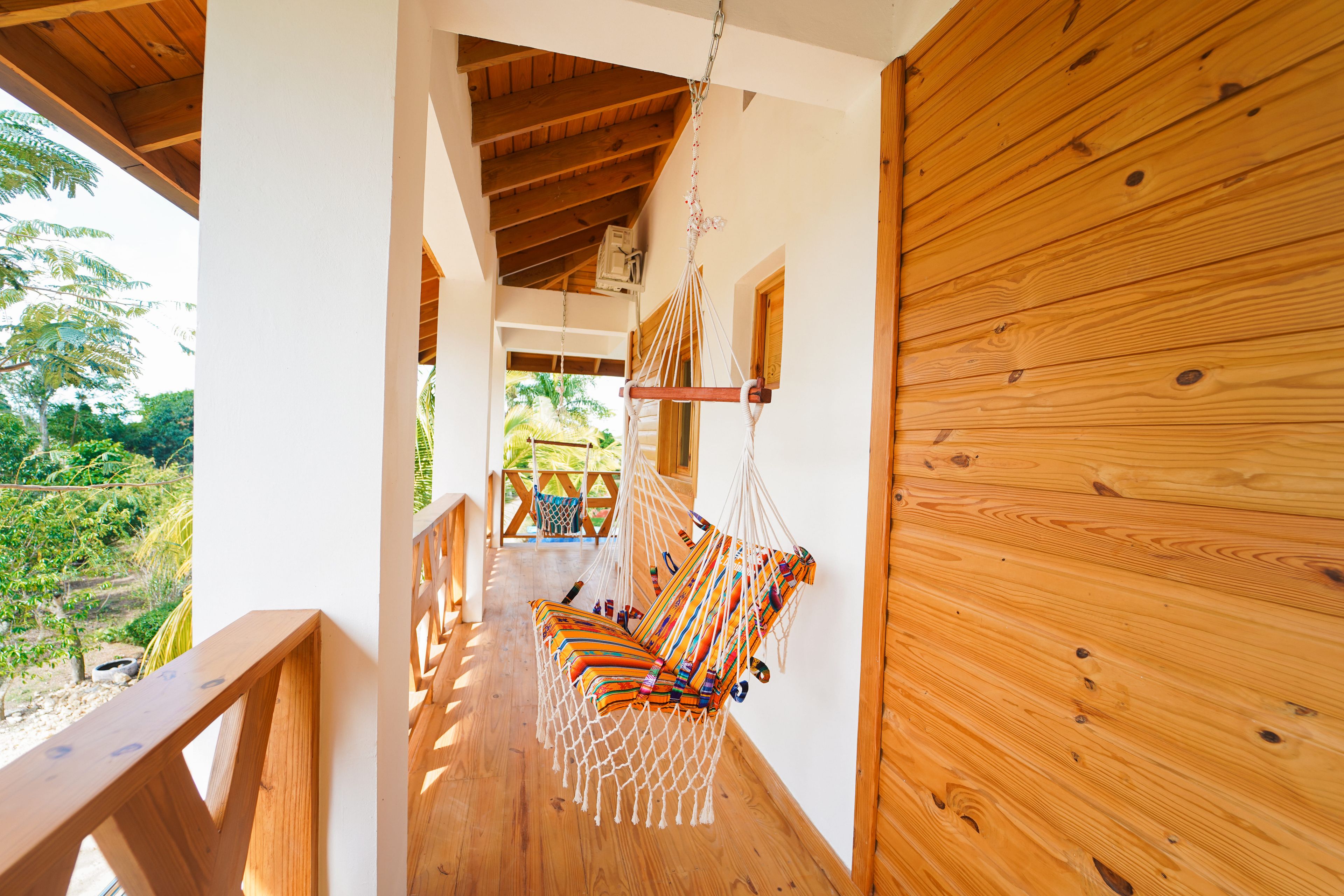 Un balcon en bois avec un fauteuil suspendu et une lampe suspendue.