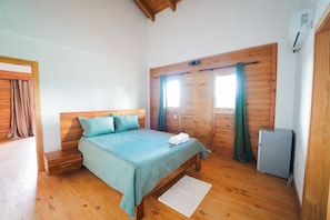 A bedroom with a wooden bed, a nightstand, a small refrigerator, and a wardrobe with a mirror.