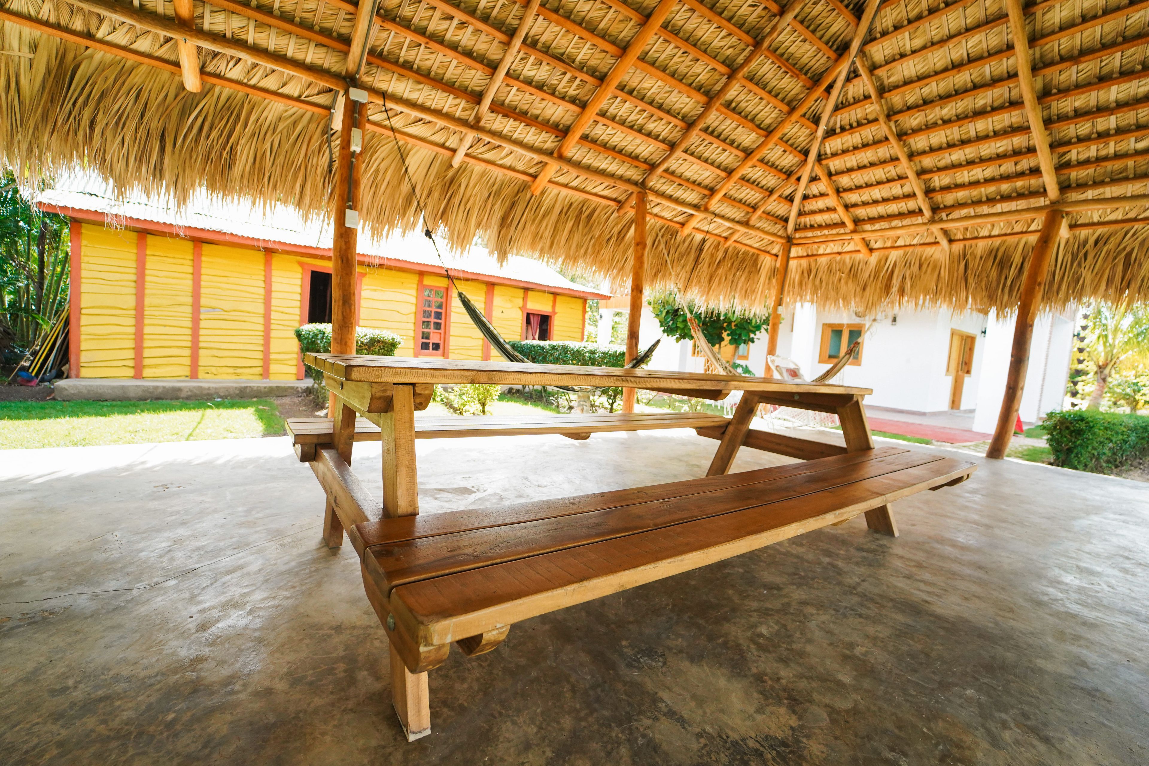 A covered outdoor seating area with a thatched roof, wooden benches, and a concrete floor.