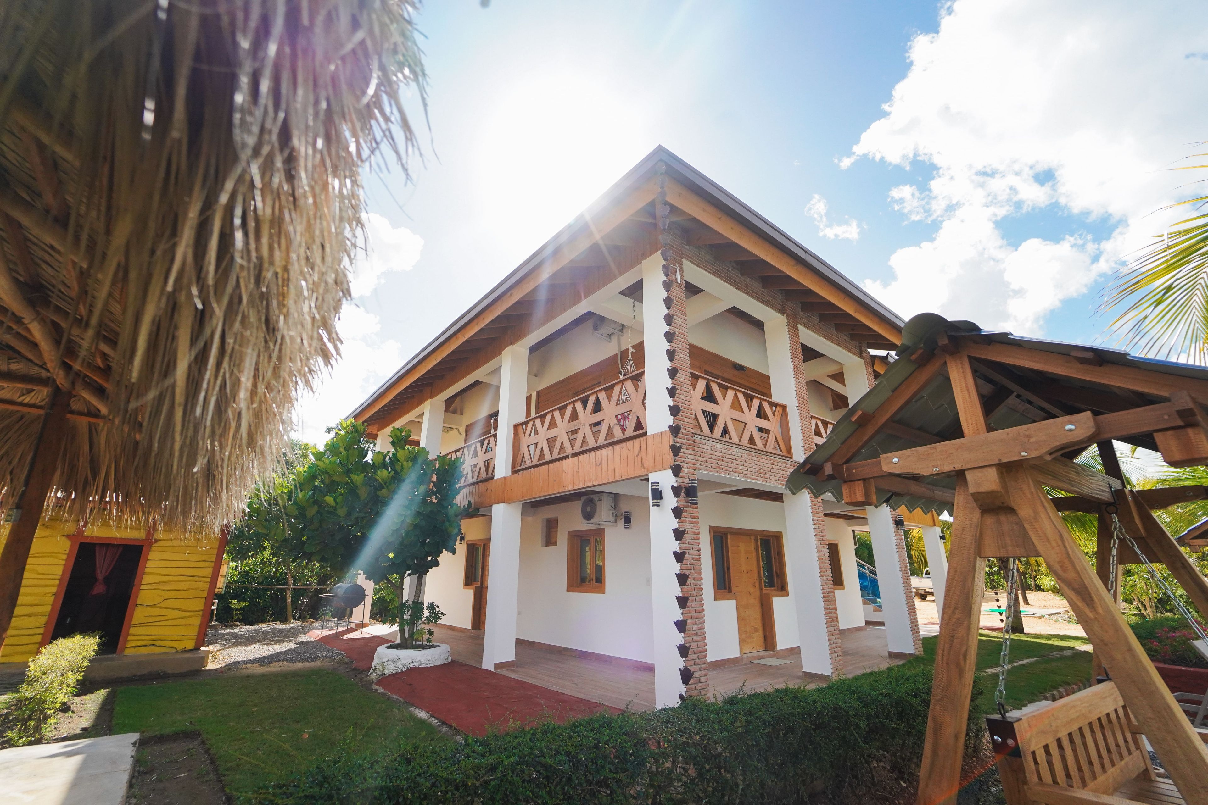 A two-story building with a balcony, a thatched roof structure, and a wooden swing set.