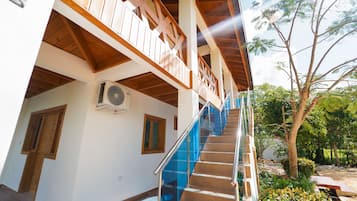 A multi-level building with wooden balconies, a staircase with blue glass railings, and a view of trees and greenery.