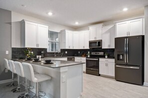 A modern kitchen with white cabinets, stainless steel appliances, and a central island with bar stools. - 9BR Luxury Villa Storey Lake Orlando (Kissimmee)