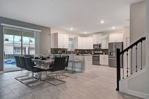 A modern kitchen with white cabinets, a central island, and a dining area with a glass partition. - 9BR Luxury Villa Storey Lake Orlando (Kissimmee)