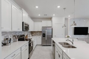 A modern kitchen with white cabinetry, stainless steel appliances, and a large island with a sink. - Luxury 5bedroom Home, Pool, Near Disney (Clermont)