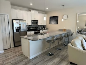 A modern kitchen with white cabinets, stainless steel appliances, a granite countertop, and a bar area with stools. - Your Orlando Home With Private Pool (Davenport)