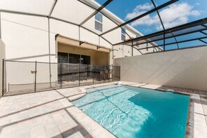 A swimming pool with a glass enclosure, a covered patio area, and a building with a garage door. - Luxury 6BR Home With Pool Solara Resort (Kissimmee)