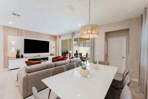 Una sala de estar moderna con un televisor de pantalla plana grande, un sofá, una mesa de comedor y una araña.