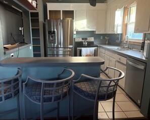 Una cocina moderna con una isla central, taburetes de bar, electrodomésticos de acero inoxidable y un ventanal que aporta luz natural.