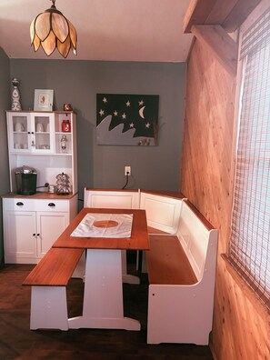 Un comedor con mesa de madera y bancos, un armario blanco con puertas de vidrio y un cuadro colgado en la pared.