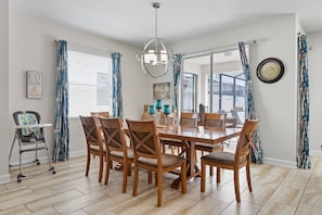 A dining room with a wooden table and chairs, a baby high chair, and a chandelier. - Storey Lake 6BR Villa w/ Private Pool & Spa (Kissimmee)