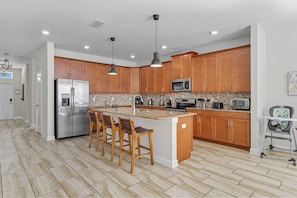A modern kitchen with wooden cabinets, stainless steel appliances, and a central island with bar stools. - Storey Lake 6BR Villa w/ Private Pool & Spa (Kissimmee)