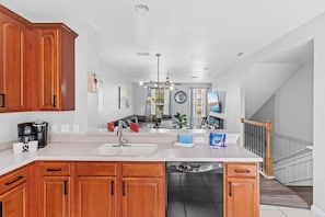 A kitchen with wooden cabinets, a white countertop, a built-in dishwasher, and a dining area with a sofa and table. - 3-bedroom Townhouse at Vista Cay Resort (Orlando)