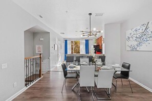 A modern dining area with a glass table and chairs, a chandelier, and a view into the kitchen. - 3-bedroom Townhouse at Vista Cay Resort (Orlando)