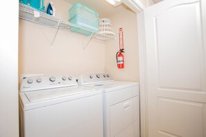 A laundry area with two Whirlpool washers, a fire extinguisher, and shelves with laundry supplies. - Compass Bay Family Comfort & Resort Amenities (Kissimmee)