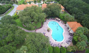 Vista aèria d'una zona residencial amb una piscina envoltada de vegetació abundant i alguns edificis amb teulades vermelles.