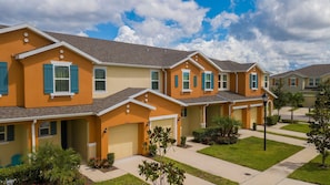 A row of townhouses with attached garages, green lawns, and a clear sky. - Compass Bay Family Comfort & Resort Amenities (Kissimmee)