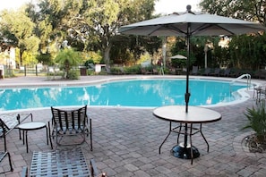 A pool area with lounge chairs, a table, and an umbrella. - Compass Bay Family Comfort & Resort Amenities (Kissimmee)