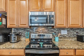 A kitchen with wooden cabinets, a stainless steel microwave, a stove, and a countertop with a knife block and a pot. - 4BR Paradise Palms Townhome, Heated Pool (Kissimmee)
