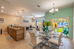 A modern kitchen with a glass dining table, a ceiling fan, and a view of a pool through a glass door. - 4BR Paradise Palms Townhome, Heated Pool (Kissimmee)