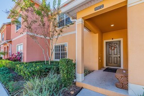 A residential building with a beige exterior, a front door with a wreath, and a small porch area. - 4BR Paradise Palms Townhome, Heated Pool (Kissimmee)
