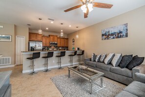 A modern kitchen with a central island, bar stools, a dining area with a grey sofa, and a painting on the wall. - 4BR Paradise Palms Townhome, Heated Pool (Kissimmee)