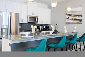 A modern kitchen with white cabinets, stainless steel appliances, and teal bar stools. - Disney 4BR Home w/ Pool + Themed Bedrooms (Kissimmee)